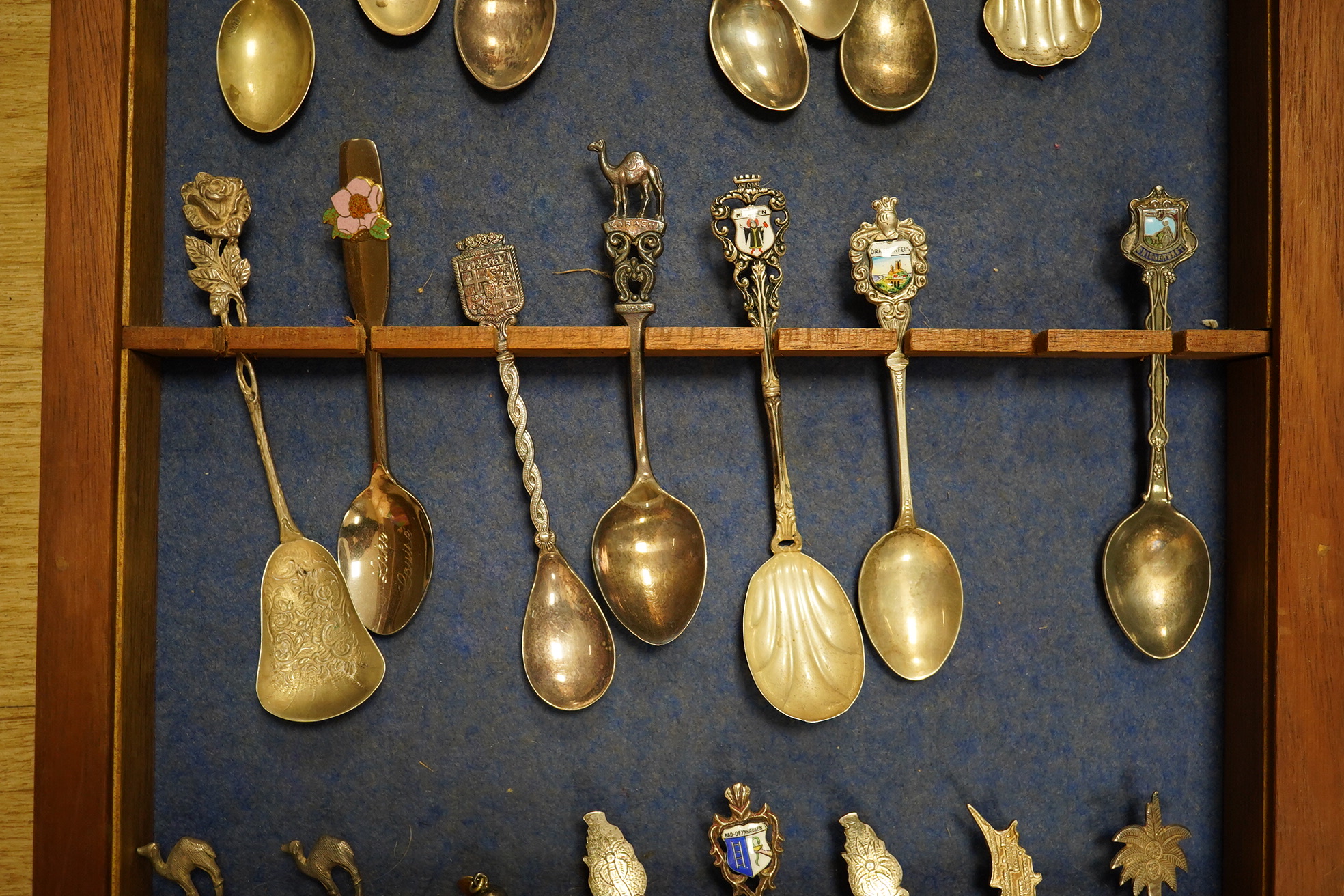 A quantity of collectors spoons from various countries, some silver with enamel, housed in a cabinet. Condition - fair